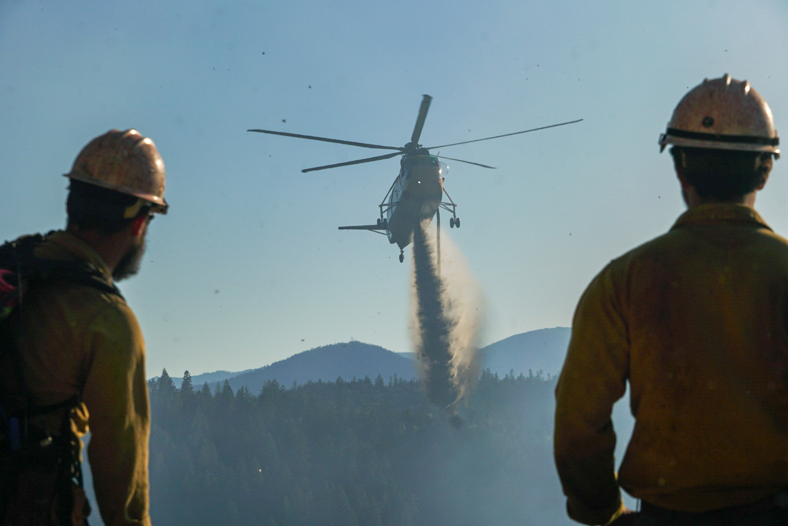 Crewmembers watch a large helicopter drop water.