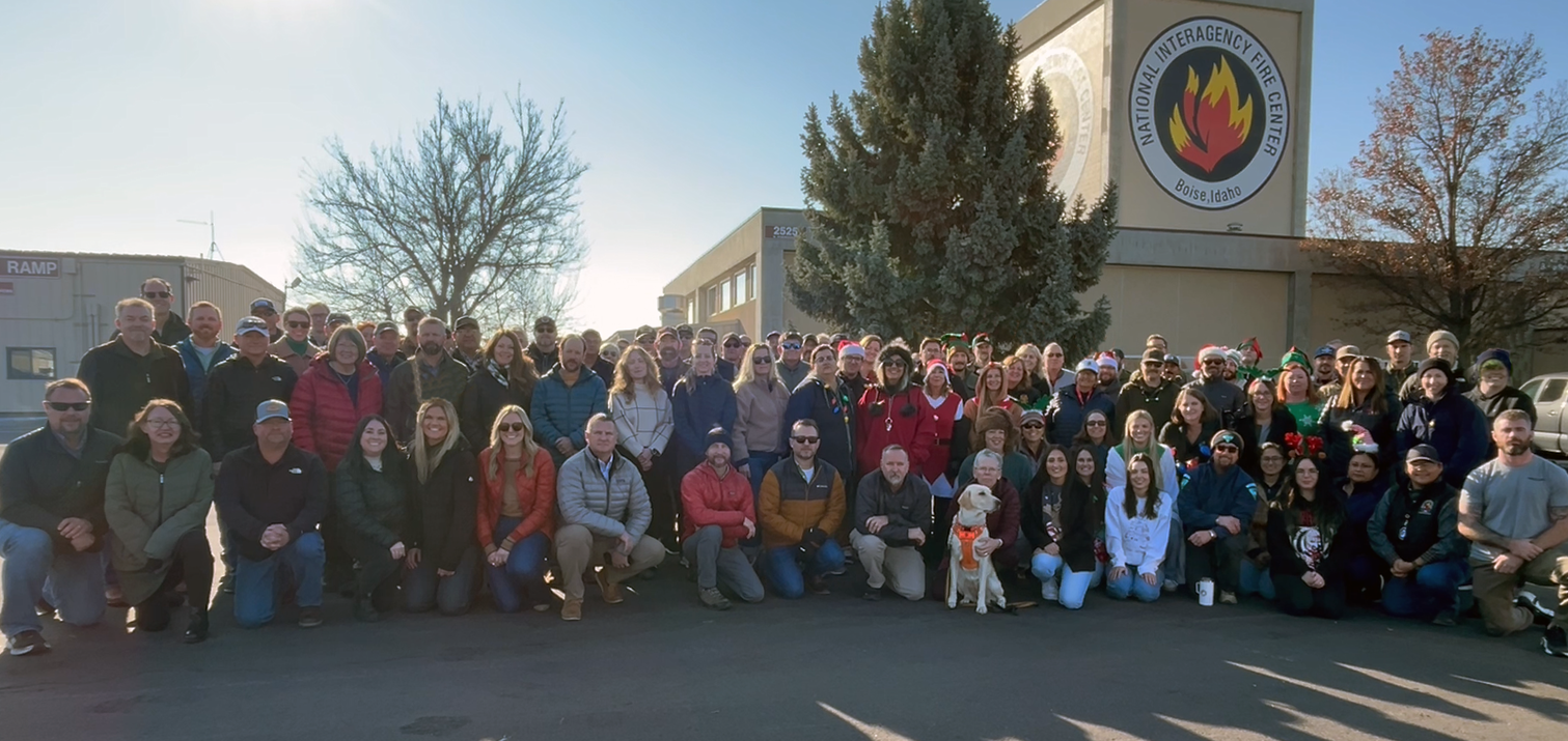 A group of about 50 people poses with the NIFC tower in the background